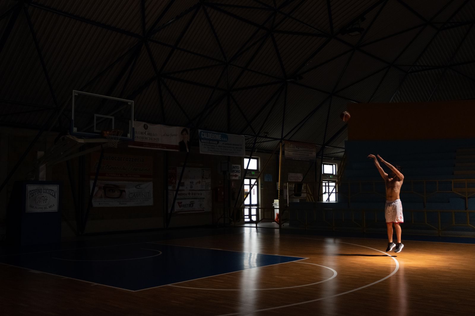 Player shooting alone in a dark gym under a single light